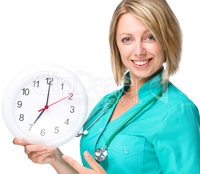 Young lady doctor is holding clock showing seven