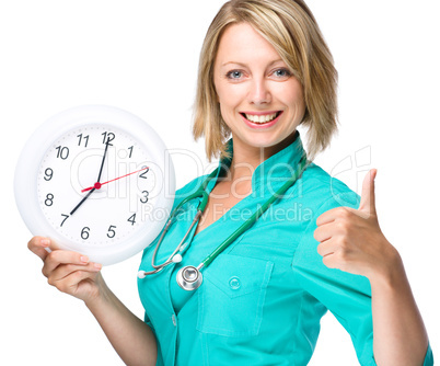 Young lady doctor is holding clock showing seven