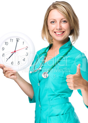 Young lady doctor is holding clock showing seven