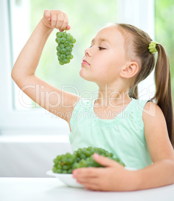 Cute little girl is eating green grapes