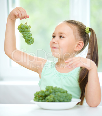 Cute little girl is eating green grapes