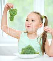 Cute little girl is looking at green grapes