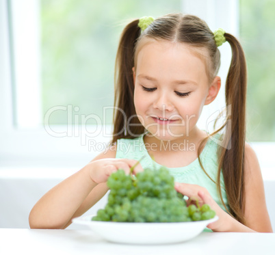 Cute little girl is eating green grapes