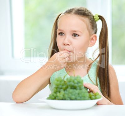 Cute little girl is eating green grapes