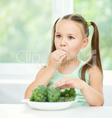 Cute little girl is eating green grapes