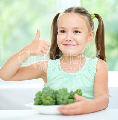 Cute little girl is eating green grapes