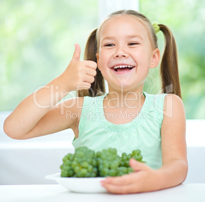 Cute little girl is eating green grapes