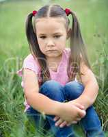 Sad little girl is sitting on green grass