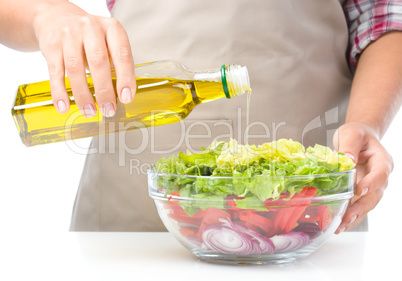 Cook is pouring olive oil into salad
