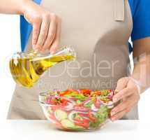 Cook is pouring olive oil into salad