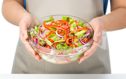 Cook is holding a big bowl with fresh salad