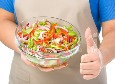 Cook is holding a big bowl with fresh salad