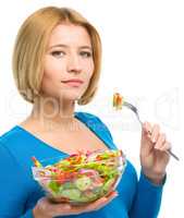 Young attractive woman is eating salad using fork