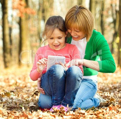 Mother is reading from tablet with her daughter