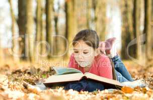 Little girl is reading a book outdoors