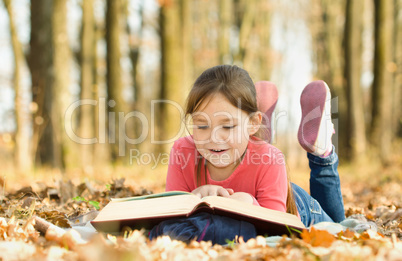 Little girl is reading a book outdoors