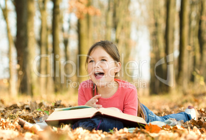 Little girl is reading a book outdoors
