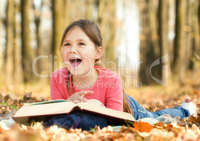 Little girl is reading a book outdoors