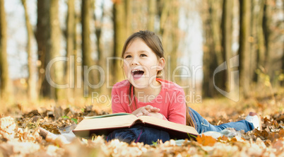 Little girl is reading a book outdoors