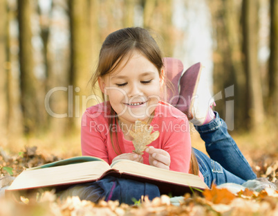 Little girl is reading a book outdoors