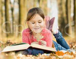 Little girl is reading a book outdoors