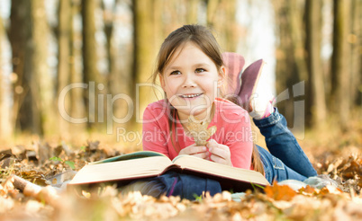 Little girl is reading a book outdoors