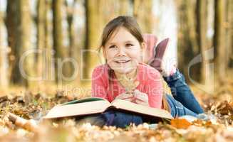 Little girl is reading a book outdoors