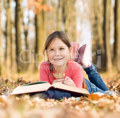 Little girl is reading a book outdoors