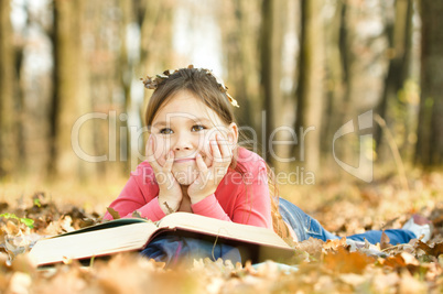 Little girl is reading a book outdoors