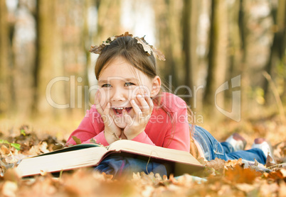 Little girl is reading a book outdoors