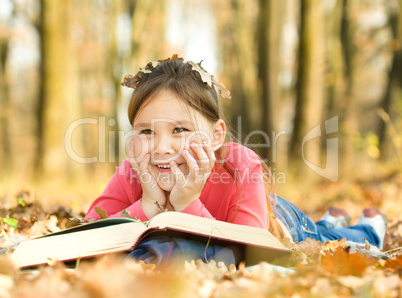 Little girl is reading a book outdoors