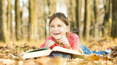 Little girl is reading a book outdoors