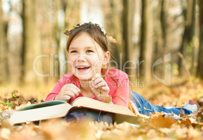 Little girl is reading a book outdoors