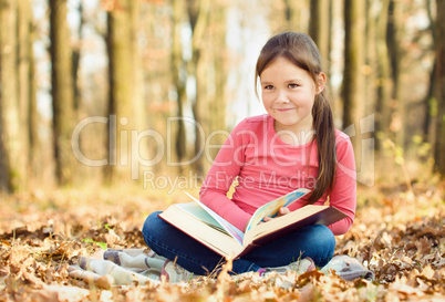 Little girl is reading a book outdoors