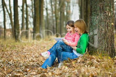 Mother and her daughter is playing with tablet