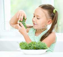 Cute little girl is eating green grapes