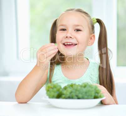 Cute little girl is eating green grapes