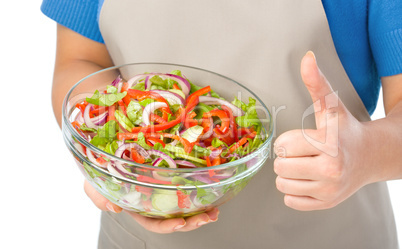 Cook is holding a big bowl with fresh salad