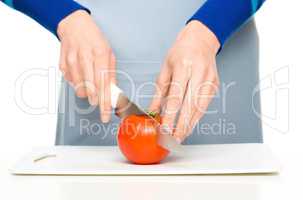 Cook is chopping red tomato