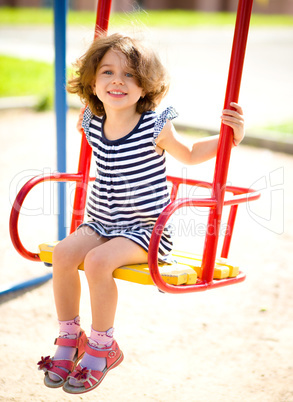 Young happy girl is swinging in playground