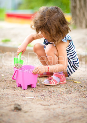 Little girl is playing with sand in playground