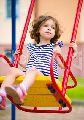 Young happy girl is swinging in playground