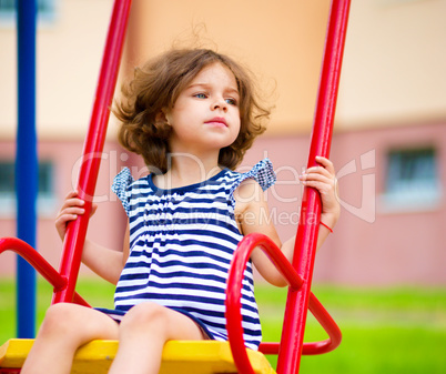 Young happy girl is swinging in playground