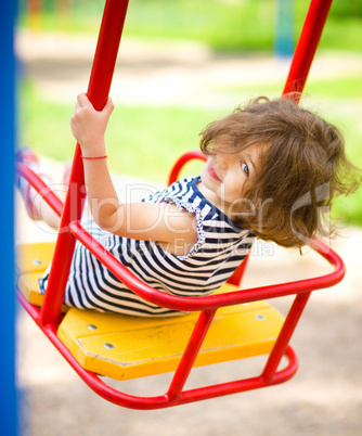 Young happy girl is swinging in playground