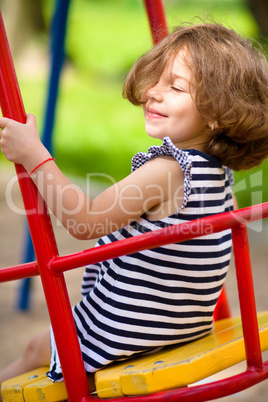 Young happy girl is swinging in playground