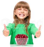 Cute girl is eating cherries showing thumb up sigh