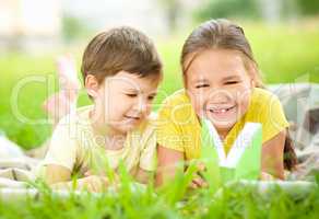 Little girl and boy are reading book outdoors