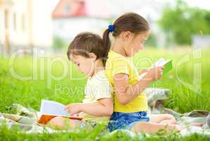 Little girl and boy are reading book outdoors