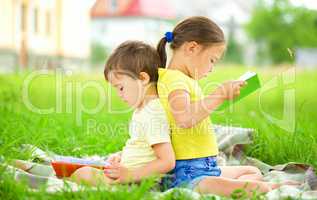 Little girl and boy are reading book outdoors