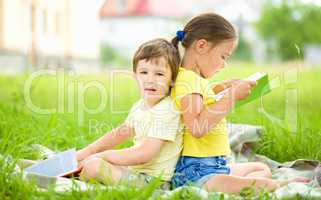 Little girl and boy are reading book outdoors